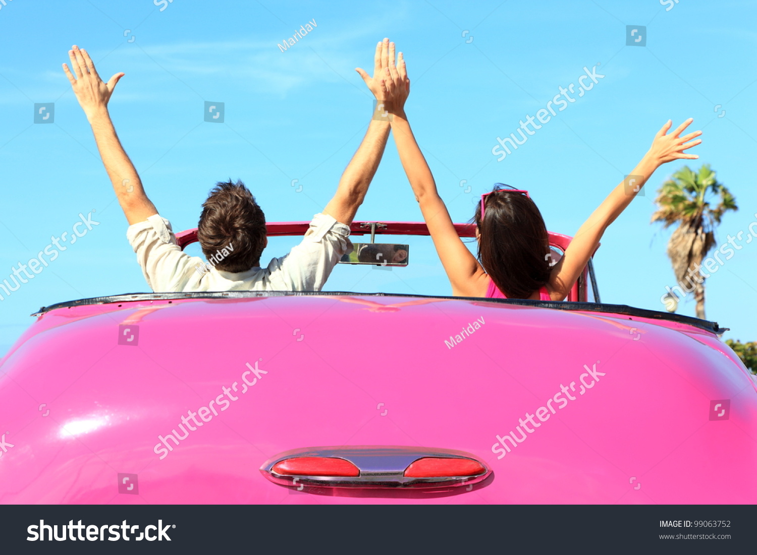 Freedom - happy free couple in car driving in pink vintage retro car cheering joyful with arms raised. Friends going on road trip travel on summer day under sun blue sky.
