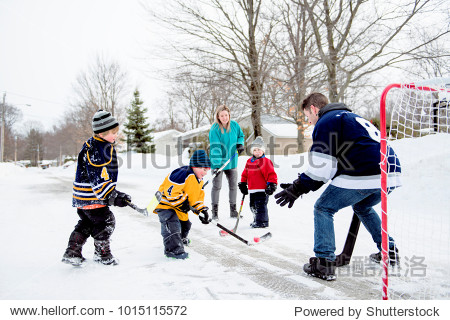 Happy funny kids playing hockey with father and mother on street in the winter season