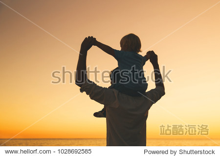Father and son silhouettes at sunset sky. Loving family and summer vacation. Man and kid boy playing together outdoors on a sea beach. Dad carrying child on his back with raised arms up on nature.
