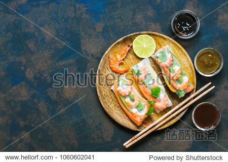 Asian food spring rolls with shrimps on a dark rustic background. Spring rolls in rice paper with a variety of sauces. Top view space for text