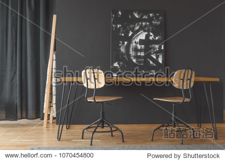 Black and white painting standing against a dark wall on a wooden dining table in monochromatic room interior