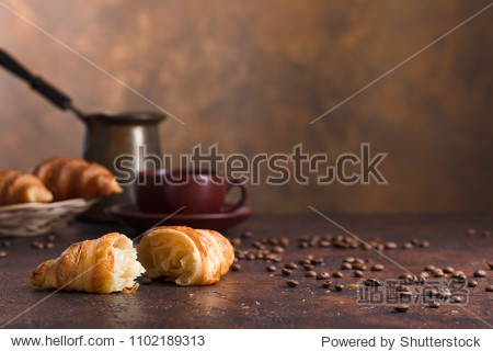 Fresh and tasty croissant and cup of coffee on old copper background. Free space for your text.