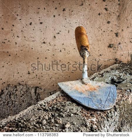 masonry trowel above a rough unfinished concrete wall