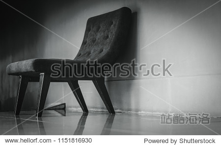 Black classic chair with unique design in empty rest room near concrete wall on dark and dramatic background. Depressed sad and lonely concept. One empty armchair in living room. Interior furniture.
