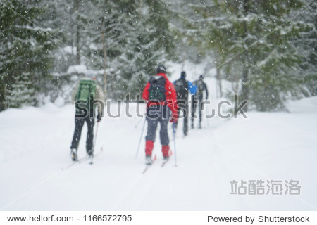 A winter snowy day and a group of skiers on road leading through the forest.  blur