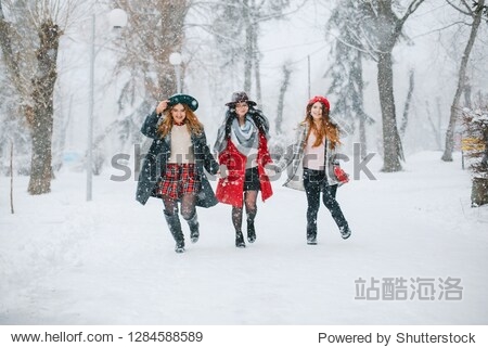 three elegant and stylish girls walking in a winter park