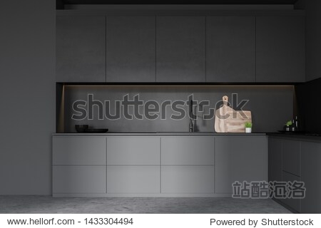 Interior of minimalistic kitchen with dark gray walls concrete floor gray countertops with built in sink and black cupboards with dishes and cutting boards. 3d rendering
