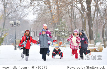 group of children and adult playing on snow in winter time  young girl pulling sister through snow on sled