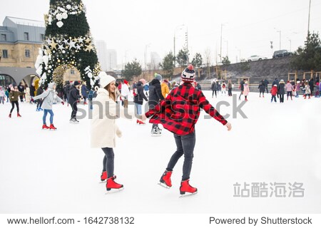 young beautiful couple boy in a red shirt and red hat girl in a white fur coat and white hat ice skating on an ice rink