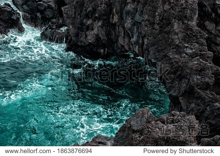 natural background. seawater naturally breaking on the strong volcanic rocks. tidewater green ocean water flow to the dark grey and black rocks. texture background and free space for designers.