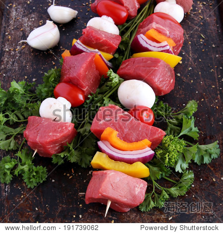 uncooked beef kebabs with vegetables and spices on brown back