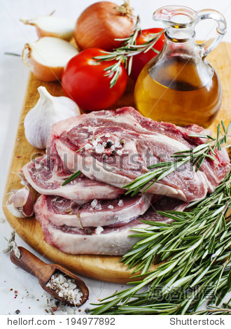 raw lamb cutlets with vegetables, herbs and spices on wooden