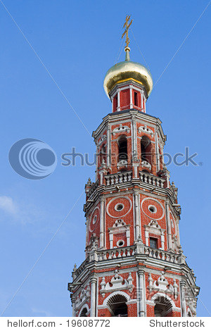 against the blue sky a high belltower from a red brick, with a