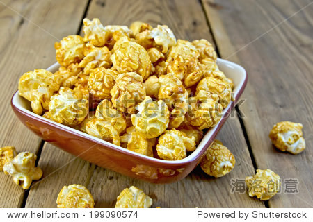 caramel popcorn in a clay bowl on a wooden boards background