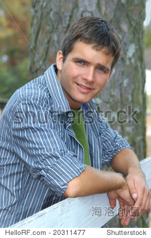 attractive male teen leans over white wooden fence.