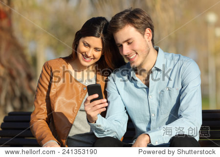 happy couple watching a smart phone sitting on a bench in a park