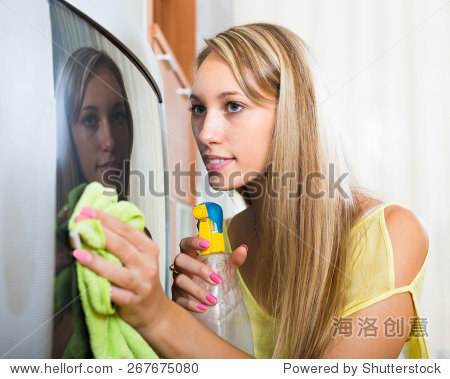 young blonde woman cleaning tv with cleanser at