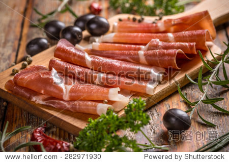 thin slices of prosciutto with olives on wooden cutting board
