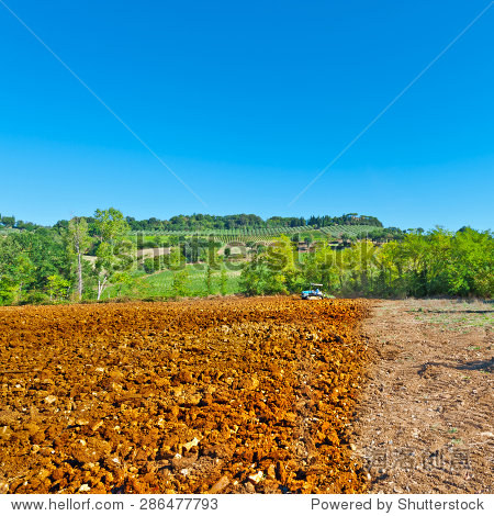 tractor plowing field on a background of vineyards in tuscany