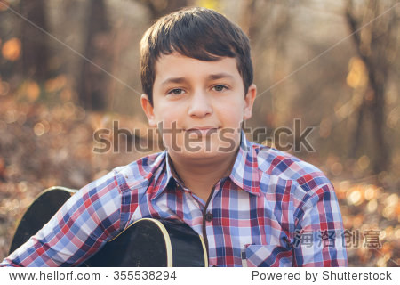 teenage boy playing guitar in a sunny autumn day