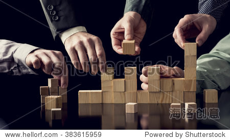 Teamwork and cooperation concept - five male hands building a structure of wooden blocks on black desk with reflection toned retro effect.