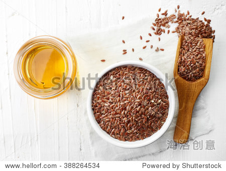 linseed oil and bowl of linseeds on white wooden background.