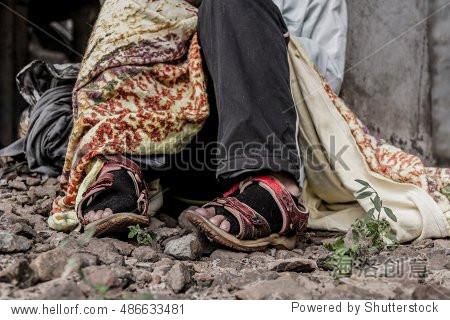 homeless woman sitting on the street wearing sandals and torn
