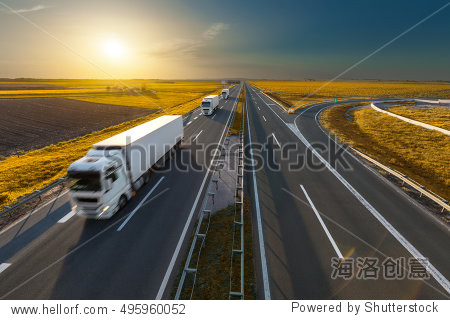 White modern delivery trucks driving towards the sun on the highway in beautiful autumn scenery. Freight scene on the motorway near Belgrade Serbia.