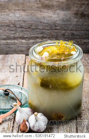 pickled gherkins in jar on rustic wooden table.