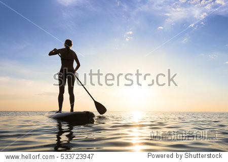 girl stand up paddle boarding (sup) on quiet sea at sunset