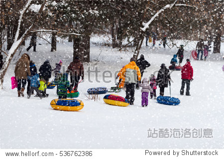 Children with parents are sleding from the hill in one of snowy park  winter leisure  active lifestyles  tobogganing  Christmas. Selective focus.