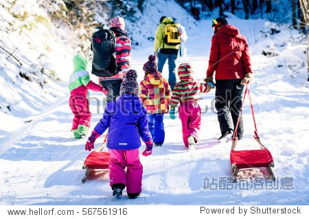 People are pulling sledge on the mountain road in woods. Active family in the winter sports activities with sleigh on snowy sliding forest road.