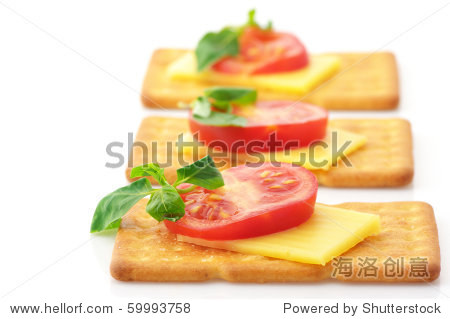 three square crackers with slices of cheese, tomato and basil