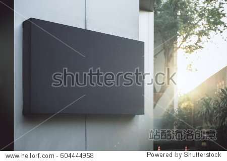 Close up of empty black poster on concrete building. Trees and sunlight in the background. Mock up