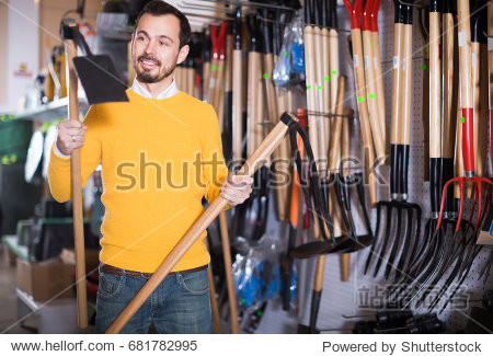 young buyer looks at the hoe and rake in a garden goods store
