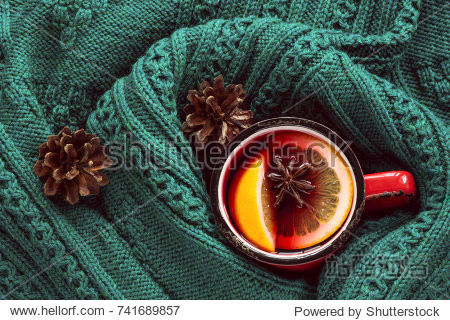 Christmas and winter traditional hot beverage. Mulled wine in red mug with spice wrapped in warm green scandinavian sweater.