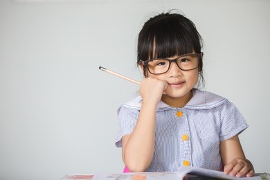 little asian kid ware glasses doing homework at home with copy space.
