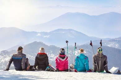 skiers looking mountain hilles while sitting on snow together, back view