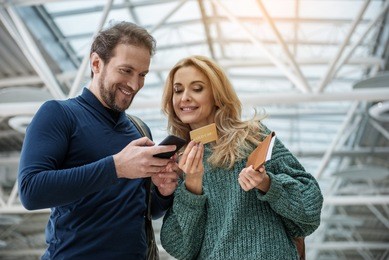 glad man and woman acquiring boarding pass for plane by mobile phone. they are looking at device