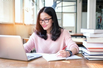 young woman taking note and using laptop while studying in library