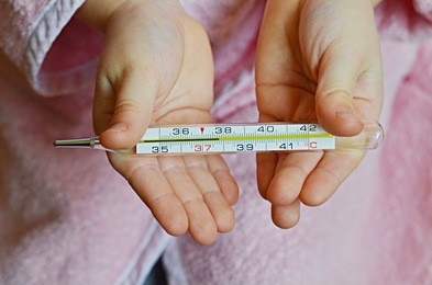little baby girl in pink bathrobe holding  thermometer with high temperature, close-up shot