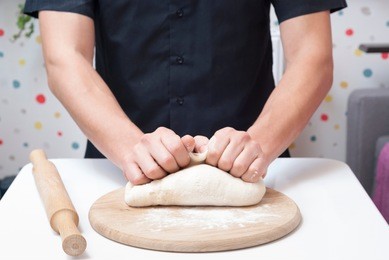chef man kneads pizza dough on the table