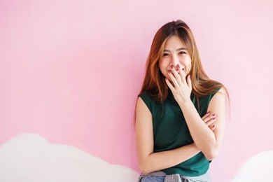 portrait of young happy woman, smiling and looking at camera, closed mouth with hand, emotional of female concept, front view