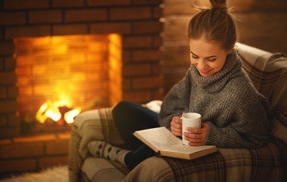 young woman enjoys reading a book by the fireplace on a winter evening
