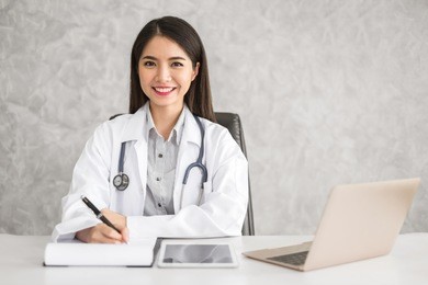 young beautiful asian doctor woman working happy and smile in hospital, sitting on table, asian medical concept