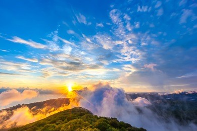 sunset hidden behind clouds and fog over hills, bright yellow sun on colorful cloudscape, blue violet orange sky. panorama of the black sea coastline from akhun mountain, big sochi, russia.