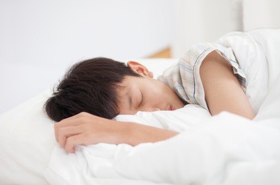 closeup of a teen boy sleeping on a bed.