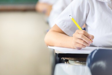 soft focus.high school or university student holding pencil writing on paper answer sheet.sitting on lecture chair taking final exam attending in examination room or classroom.student in uniform