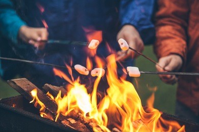 hands of friends roasting marshmallows over the fire in a grill closeup
