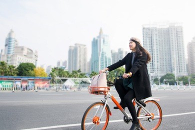 asian office lady riding public bicycle through urban area